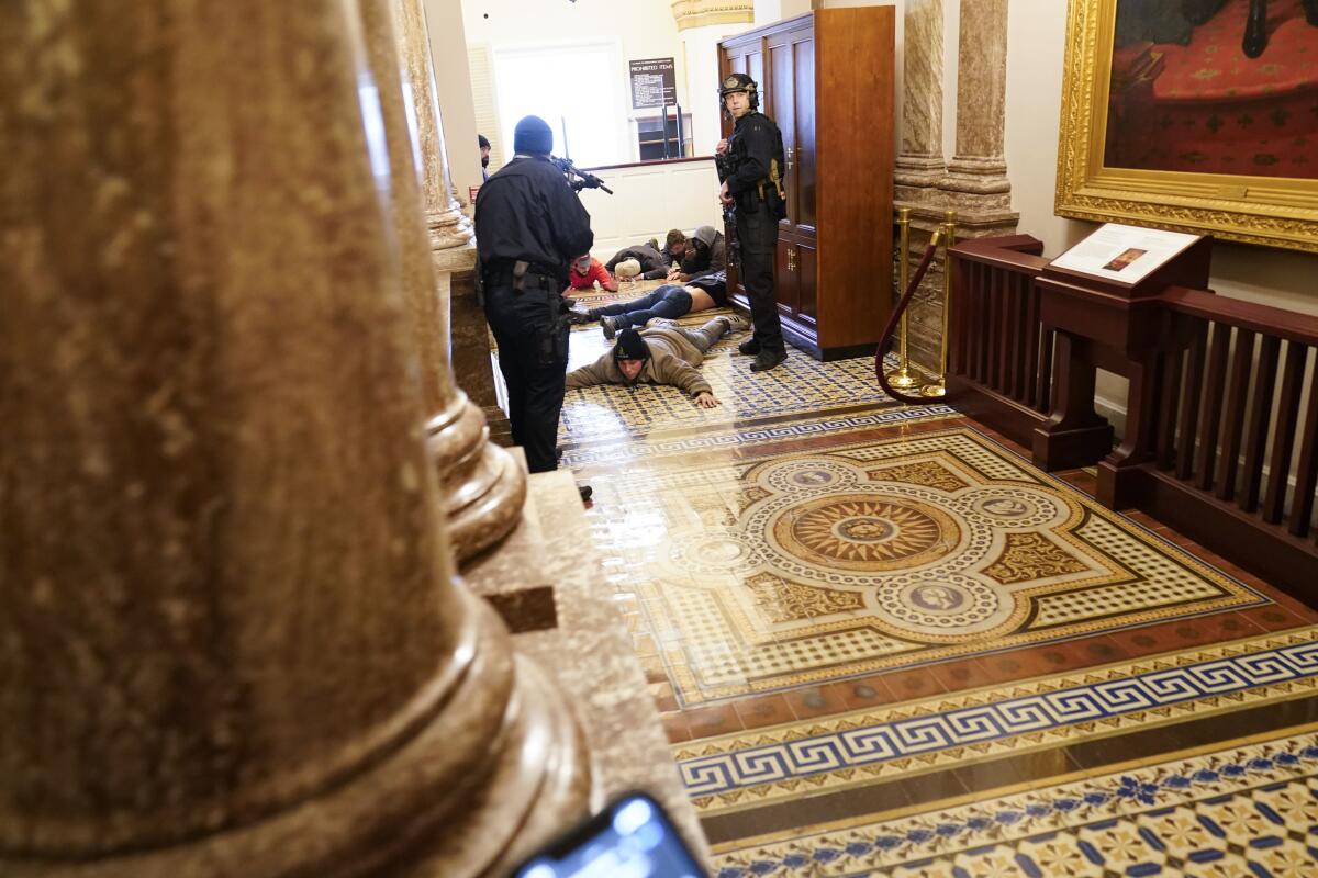 People lie on the floor of a Capitol hallway as police officers aim weapons