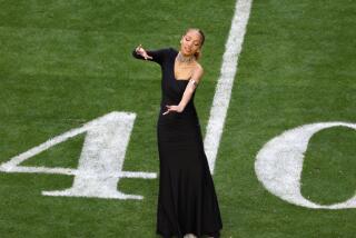 A full-body view of a young woman in long black dress gesturing with her arms while performing on a football field