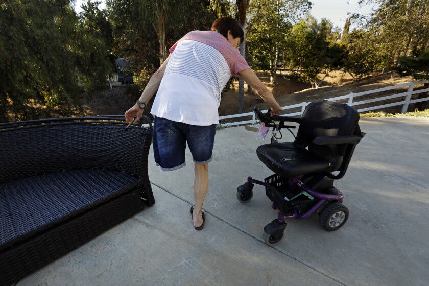 A woman with one leg stands by a motorized wheelchair.