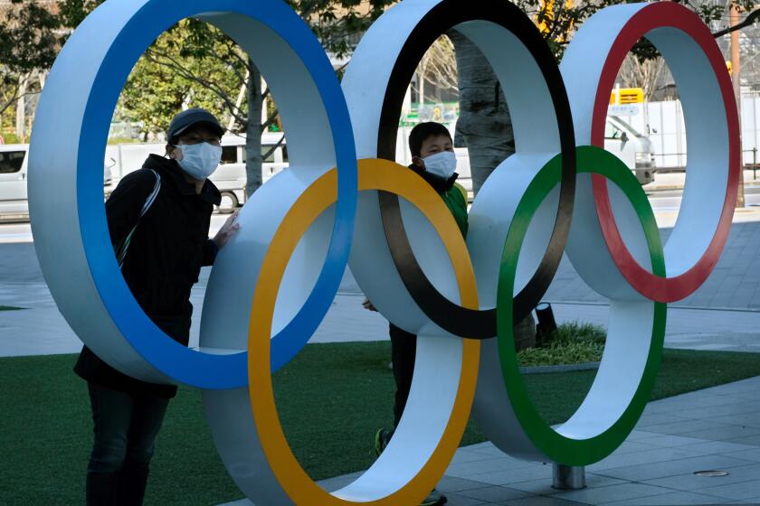 Pedestrians pose with an installation of the Olympic rings in Tokyo on March 24, 2020. - The International Olympic Committee came under pressure to speed up its decision about postponing the Tokyo Games on March 24 as athletes criticised the four-week deadline and the United States joined calls to delay the competition. (Photo by Kazuhiro NOGI / AFP) (Photo by KAZUHIRO NOGI/AFP via Getty Images)