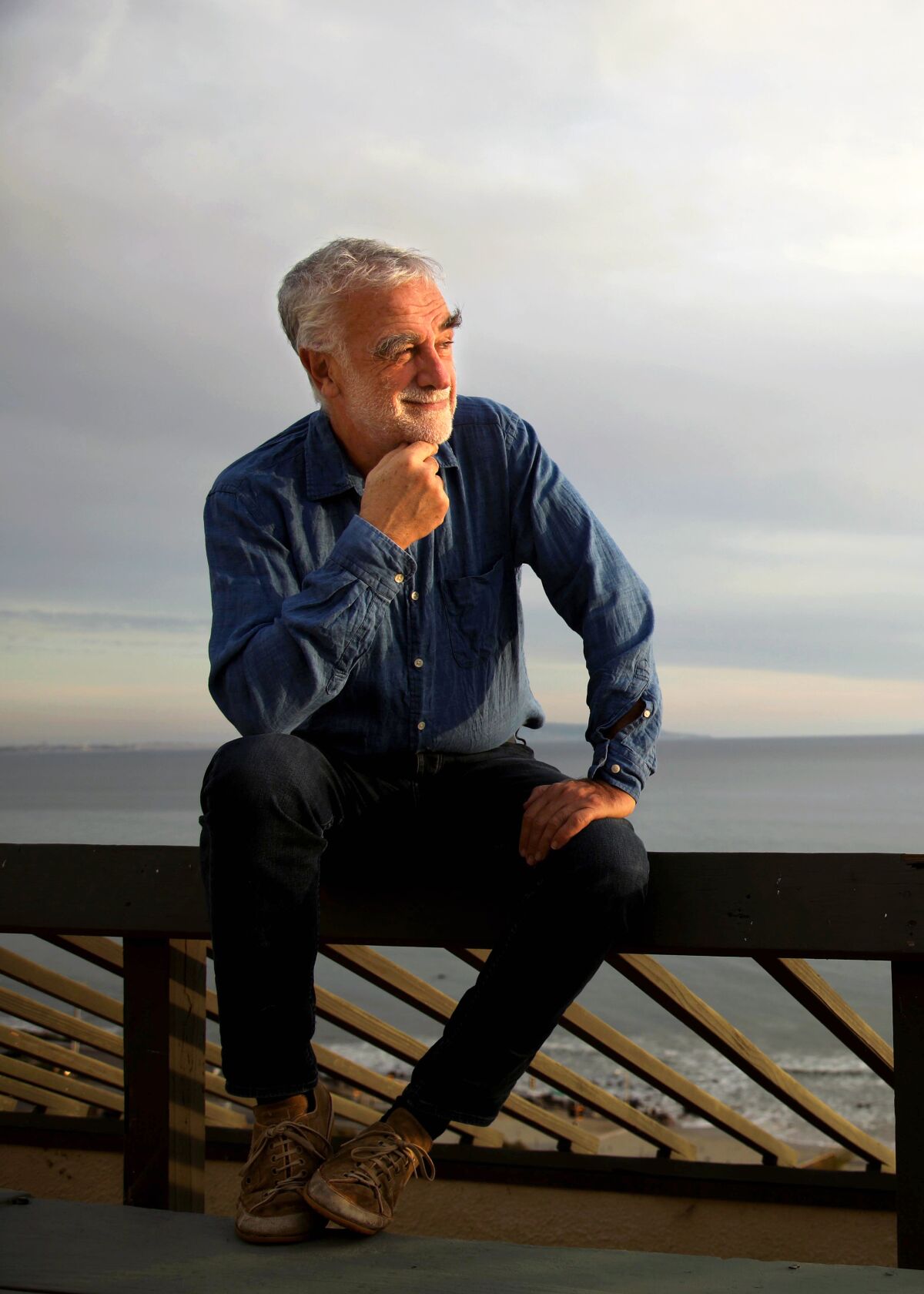 Luis Moreno Ocampo, éclairé par la lumière chaude du coucher du soleil, est assis sur la balustrade d'un patio, regardant vers la droite.  La mer calme est derrière.