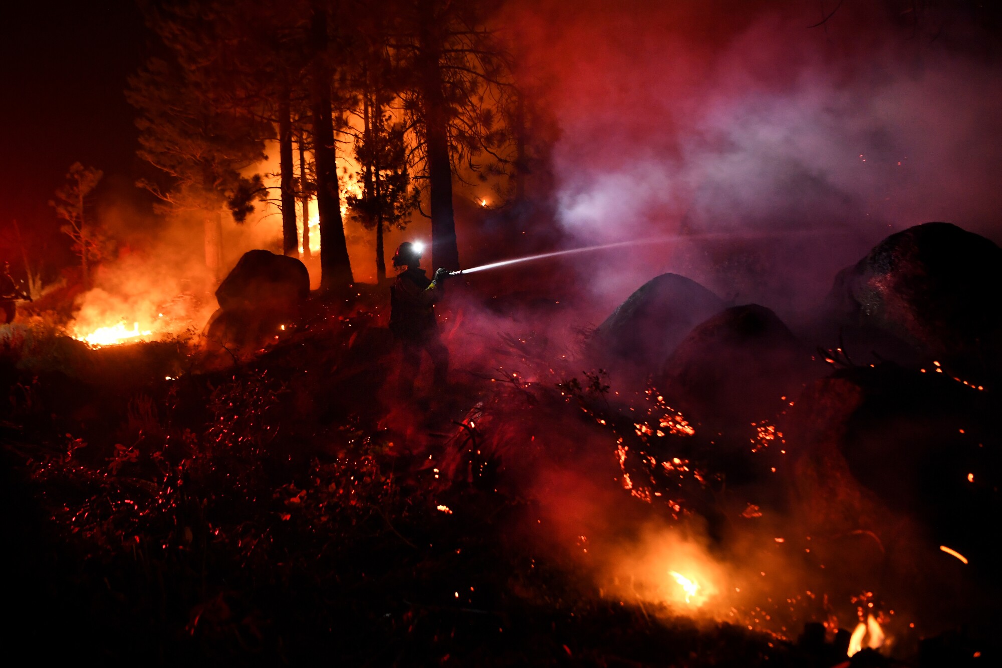 A firefighter sprays water onto a fire surrounded by smoke.