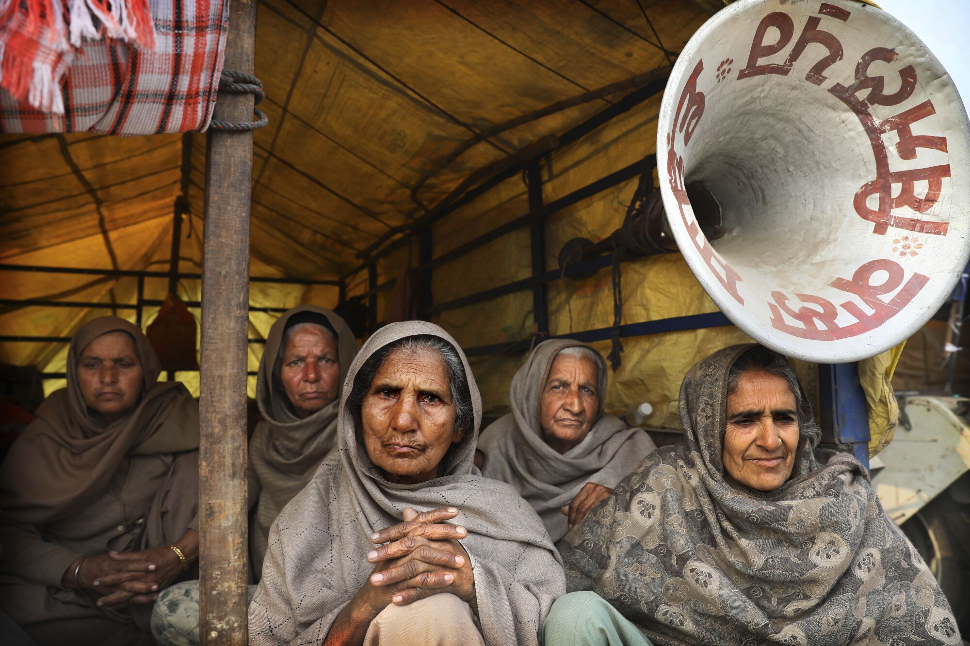 Elderly female farmers sit at the back of a trailer as they participate in a protest against new farm laws
