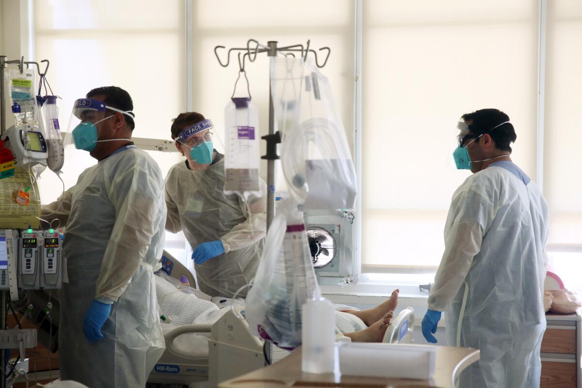 Healthcare workers in protective gear surround a patient in a hospital bed