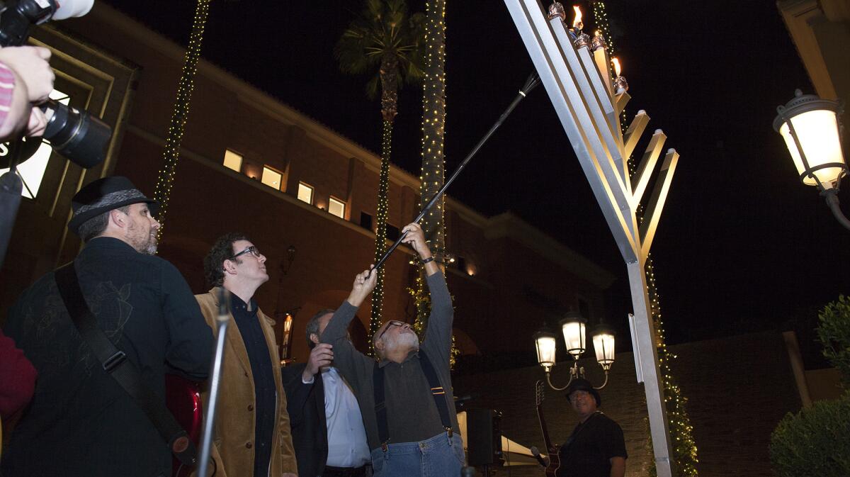 Honorary guest Sam Silberberg, 87, a Holocaust survivor, lights candles atop a large menorah during a Hanukkah ceremony Wednesday evening at Fashion Island in Newport Beach.