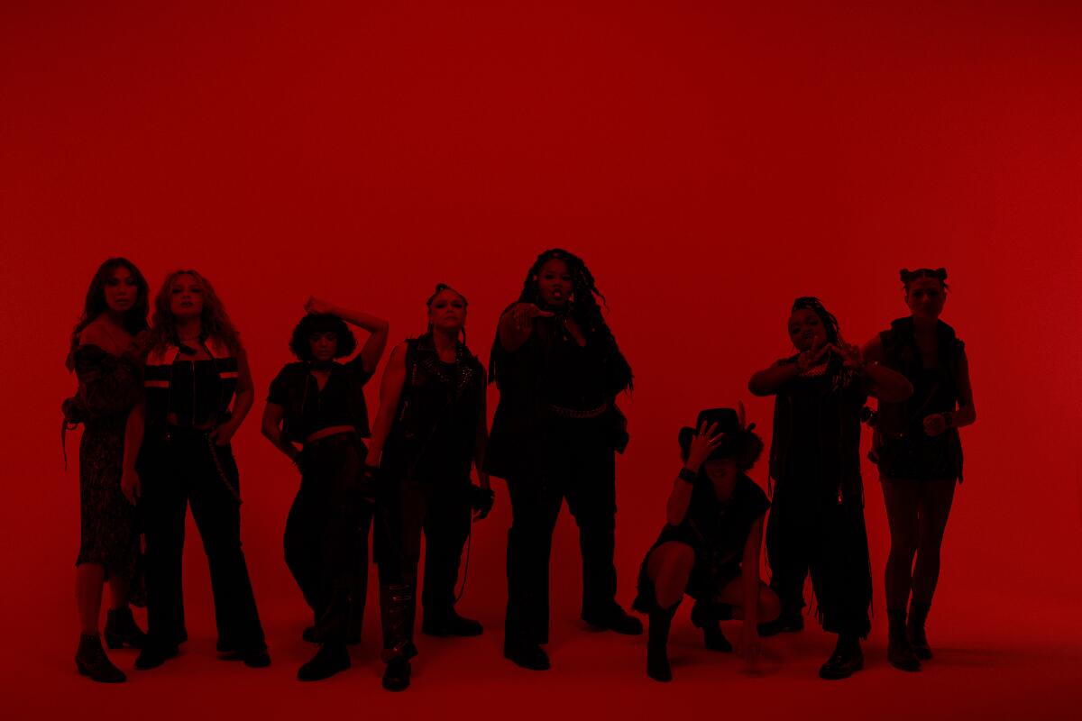 A line of actors in dark clothing standing against a red background