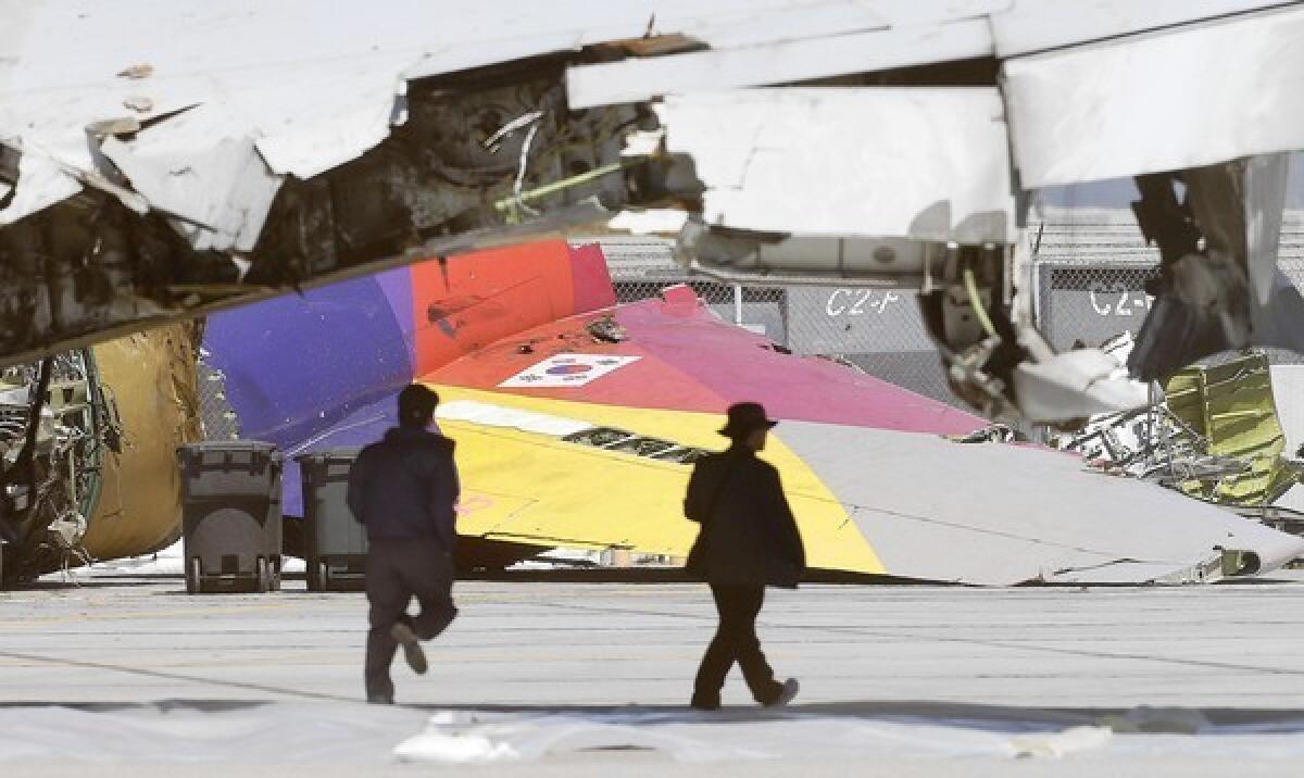 Two men walk past the wreckage of Asiana Airlines Flight 214 at San Francisco International Airport. The July 6 crash has brought renewed scrutiny to foreign airlines' safety and training procedures.