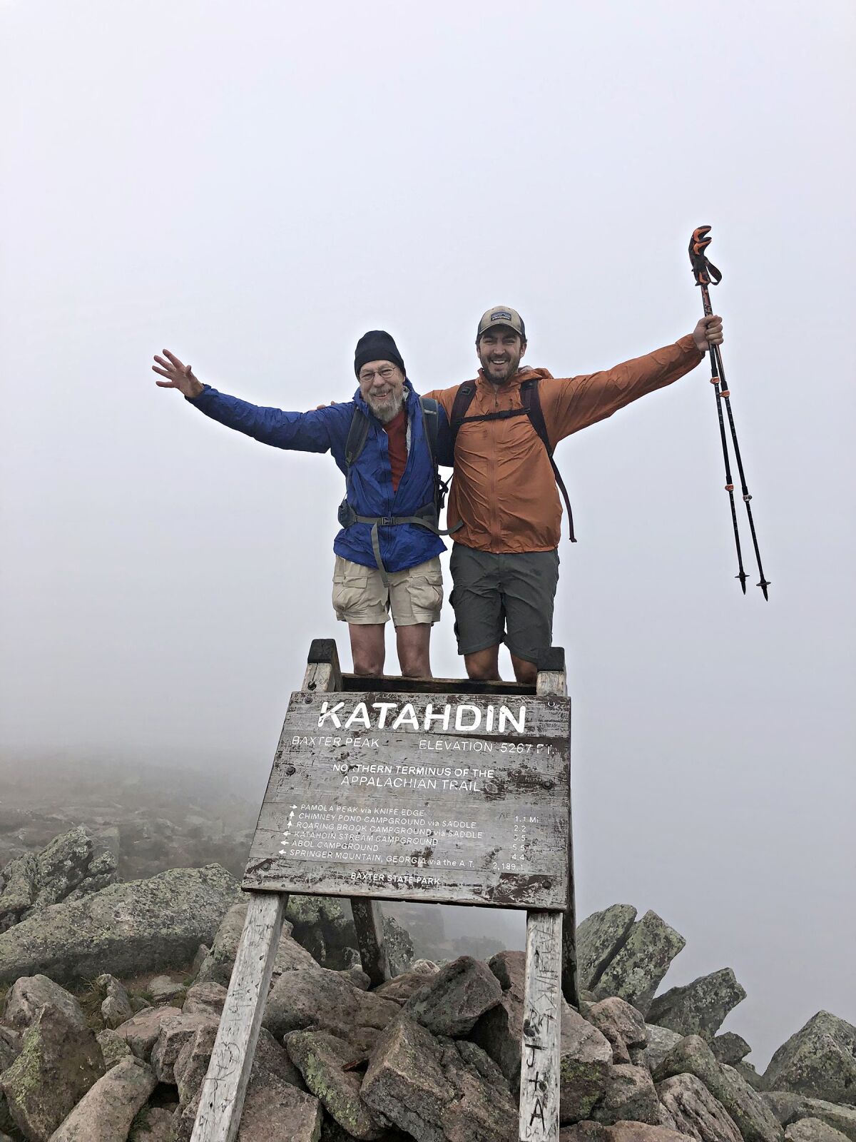 Two men with their arms raised by a sign that says Katahdin