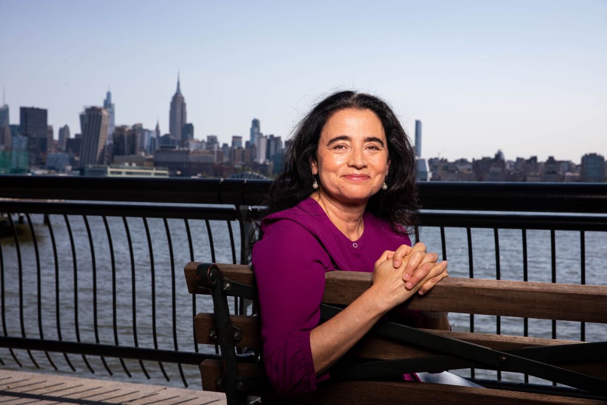 Patricia Cardoso, director of "Real Women Have Curves," sits on a bench in front of a city skyline. 