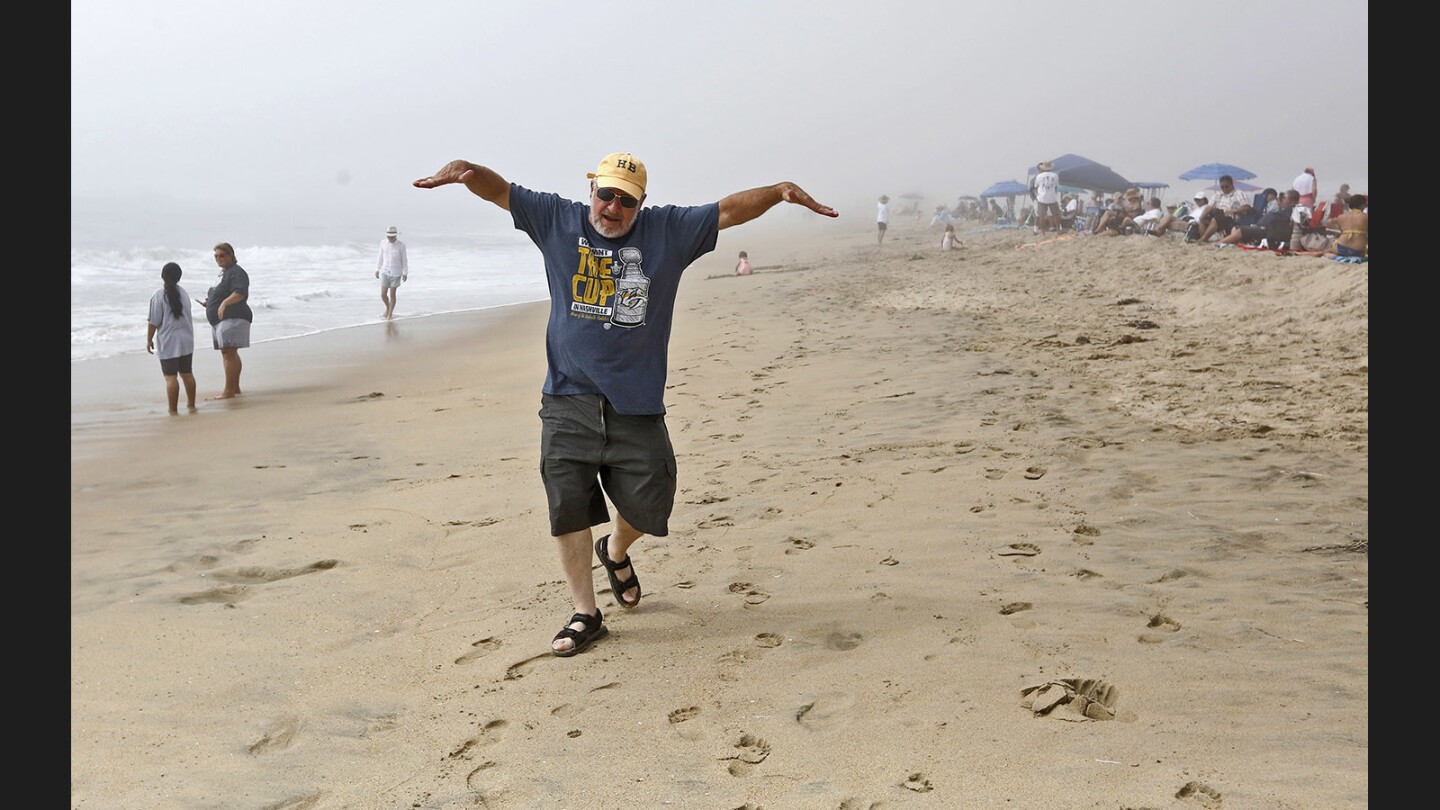 A man pretends to be an airplane as people wait Friday for the Breitling Huntington Beach Airshow practice to start. The practice was called off because of the marine layer.