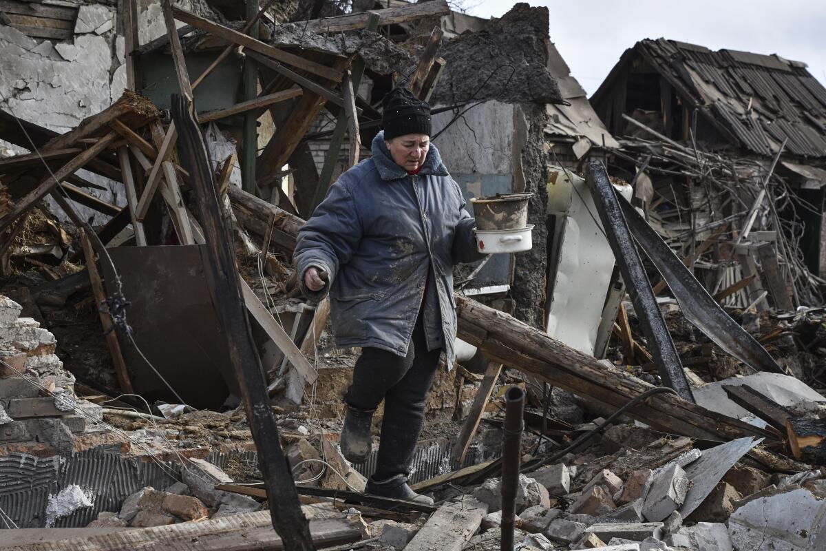 A Ukrainian woman carries possessions rescued from the rubble of her house destroyed by a Russian drone.