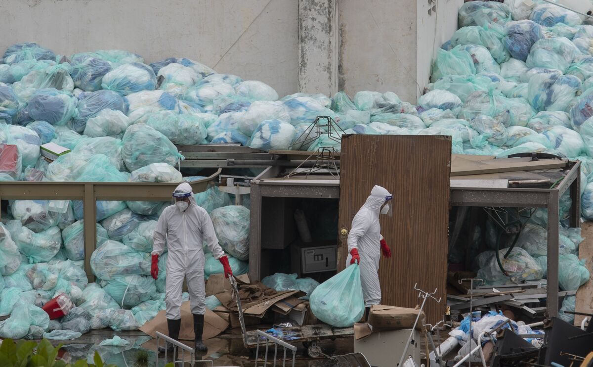 Medical workers using protective equipment dispose of trash bags containing hazardous biological waste into a large pile outside the Hospital del Instituto Mexicano del Seguro Social, which treats patients with COVID-19 in Veracruz, Mexico, Wednesday, Aug. 12, 2020. Improper disposal of medical waste has become an increasing problem in Mexico amid the pandemic. (AP Photo/Felix Marquez)