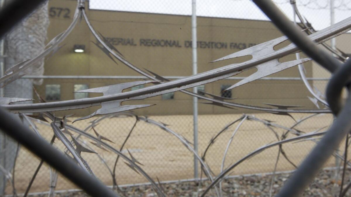 With razor wire in foreground, a building is seen with words on it reading, "Imperial Regional Detention Facility"