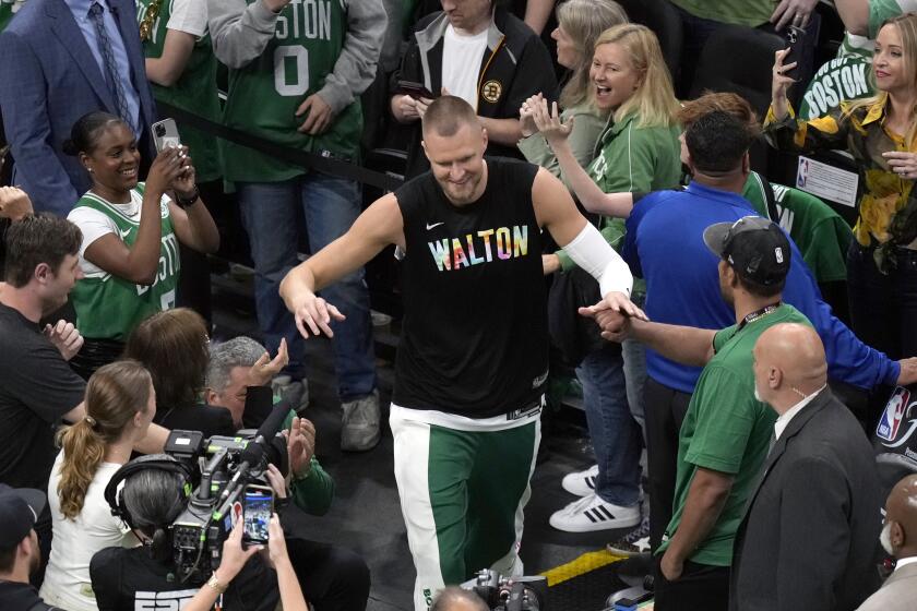 Boston Celtics center Kristaps Porzingis heads to the court while wearing a warmup shirt honoring basketball great Bill Walton before Game 1 of the basketball team's NBA Finals against the Dallas Mavericks, Thursday, June 6, 2024, in Boston. (AP Photo/Michael Dwyer)