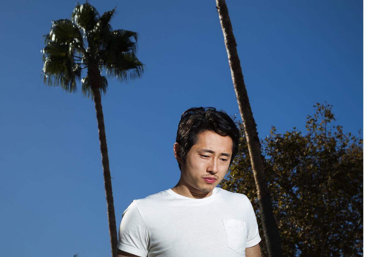 Steven Yeun in a white T-shirt with palm trees in the background