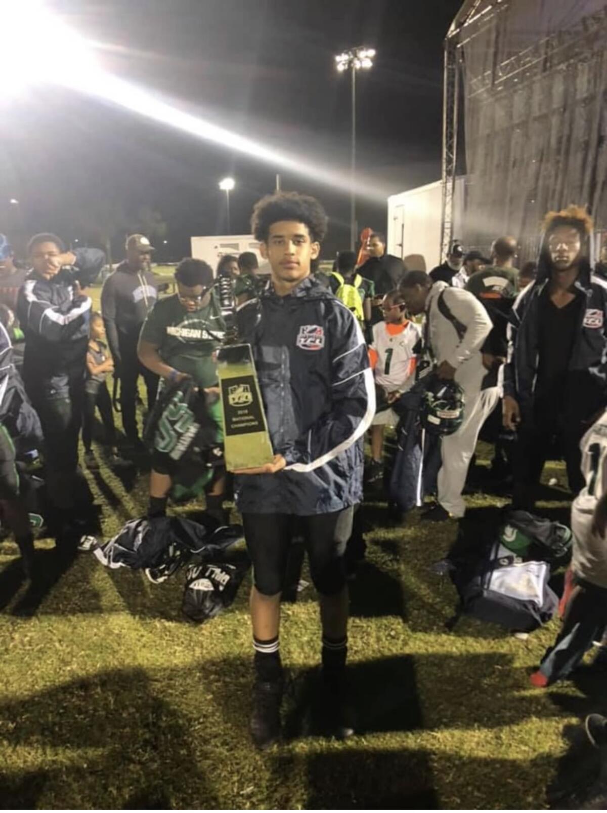 Dante Moore holds a youth football national championship trophy.