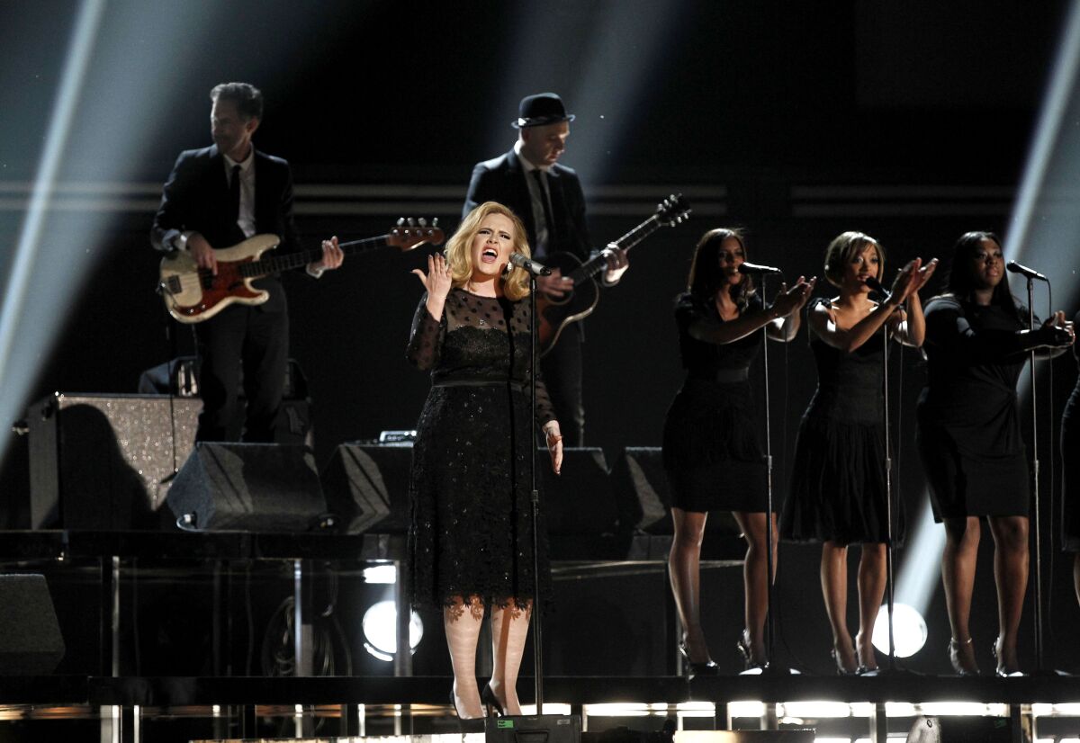 A woman in black sings onstage with a band and backup singers behind her