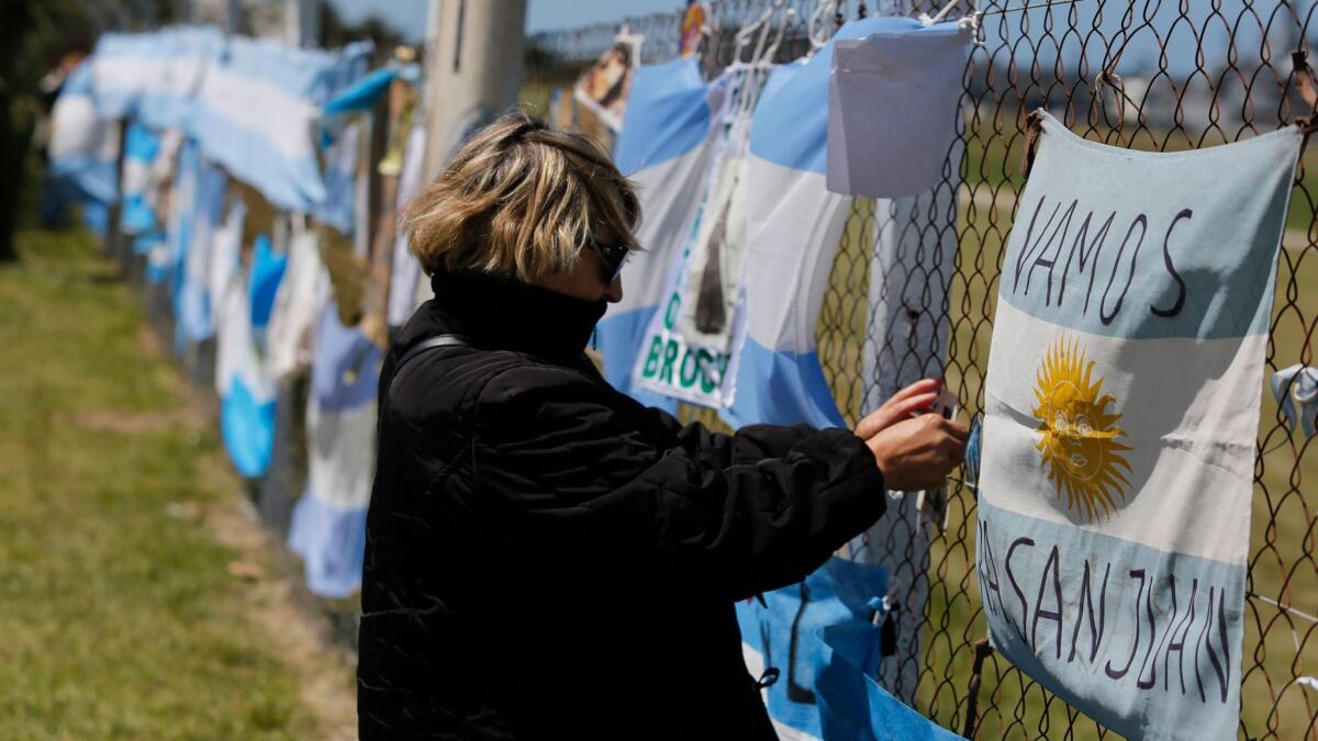 A woman stand before a fence blanketed with national flags, in support of the crew members of the lost submarine.
