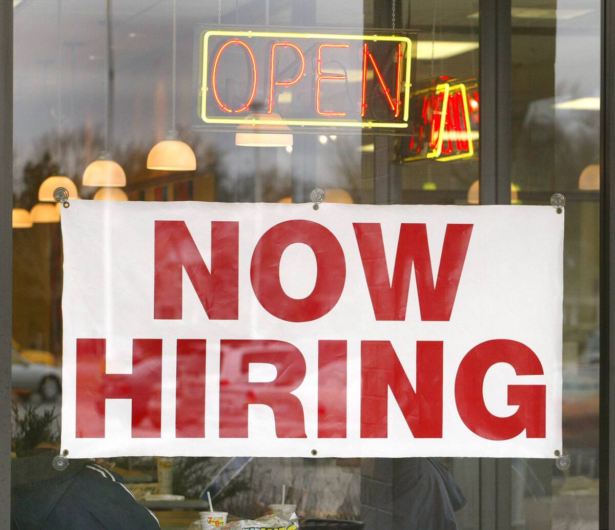 "Now Hiring" signage is visible in the window of a Subway restaurant.