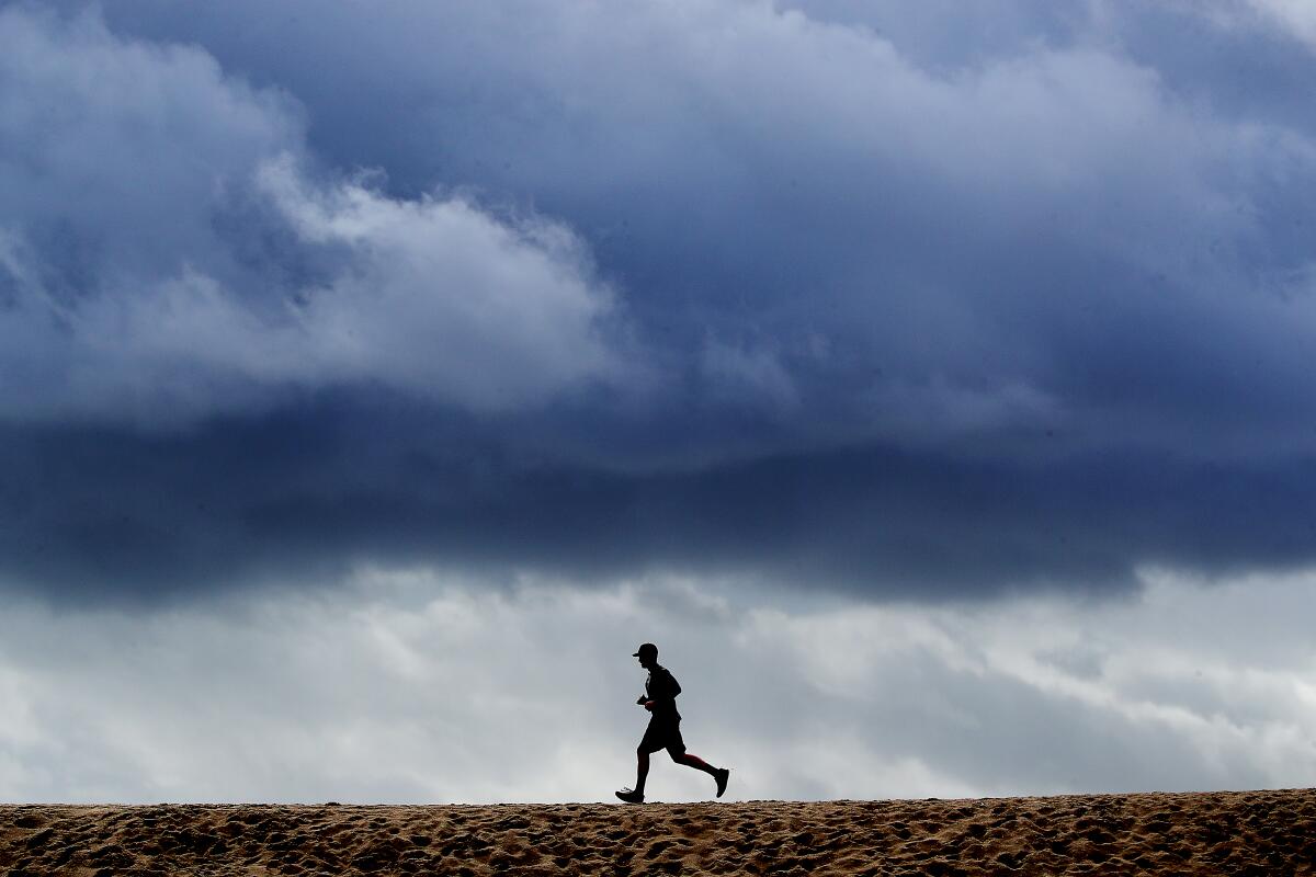 A man runs while a storm drifts over Seal Beach.