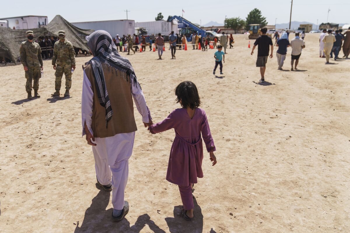 A man walks with a child through Fort Bliss' Doña Ana Village where Afghan refugees are being housed, in New Mexico, Friday, Sept. 10, 2021. The Biden administration provided the first public look inside the U.S. military base where Afghans airlifted out of Afghanistan are screened, amid questions about how the government is caring for the refugees and vetting them. (AP Photo/David Goldman)