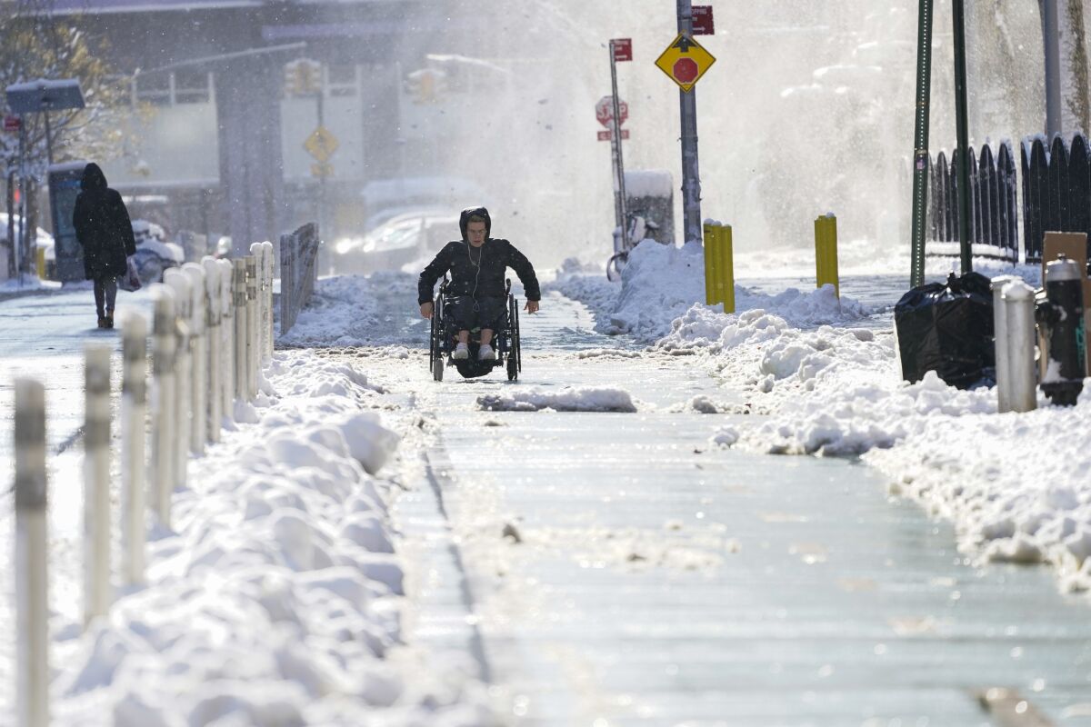 A person on a wheelchair uses the bike lane to navigate the snow covered streets in lower Manhattan, Friday, Jan. 7, 2022, in New York. A winter storm that has already left areas of the south with more than 6 inches of snow moved into the northeast during the morning commute and prompted many school districts to close for the day. (AP Photo/Mary Altaffer)