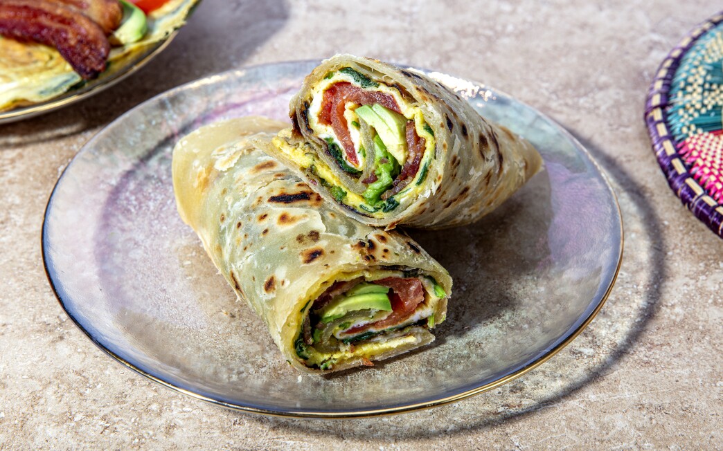 An omelet cooked with spinach is spiraled inside chapati and stuffed with avocado and bacon.