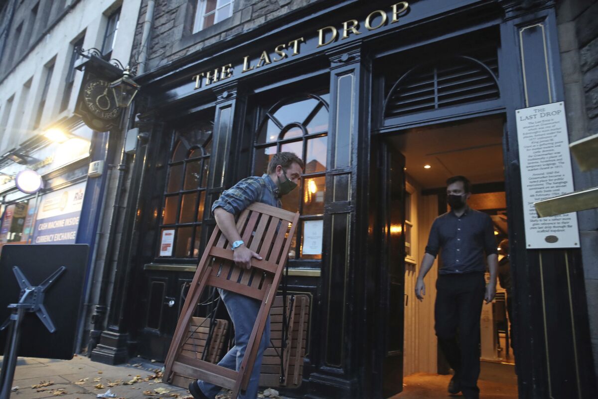 A man stacks away chairs outside The Last Drop pub, as temporary restrictions announced by First Minister Nicola Sturgeon to help curb the spread of coronavirus have come into effect from 6pm, in Edinburgh, Friday, Oct. 9, 2020. (Andrew Milligan/PA via AP)
