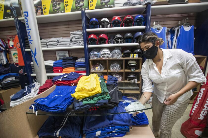 BOYLE HEIGHTS, CA-MAY 27, 2020: Daniela Prieto, 21, an employee at Deportes Prieto, a retail business on 1st St. in Boyle Heights, disinfects inside the store that is currently only allowing customers to pre-order merchandise and pick up at the store. The business re-opened on Monday with curbside pick-up only after previously being closed due to the coronavirus. (Mel Melcon/Los Angeles Times)