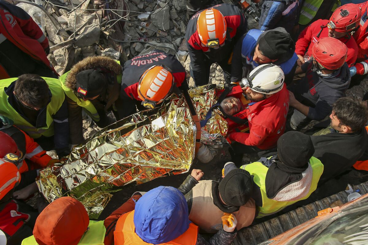 Turkish rescue workers carry a man wrapped in a blanket after pulling him from rubble.