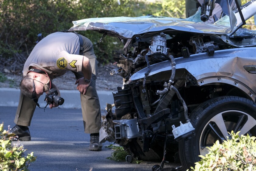A law enforcement officer looks over a damaged vehicle following a rollover accident involving golfer Tiger Woods