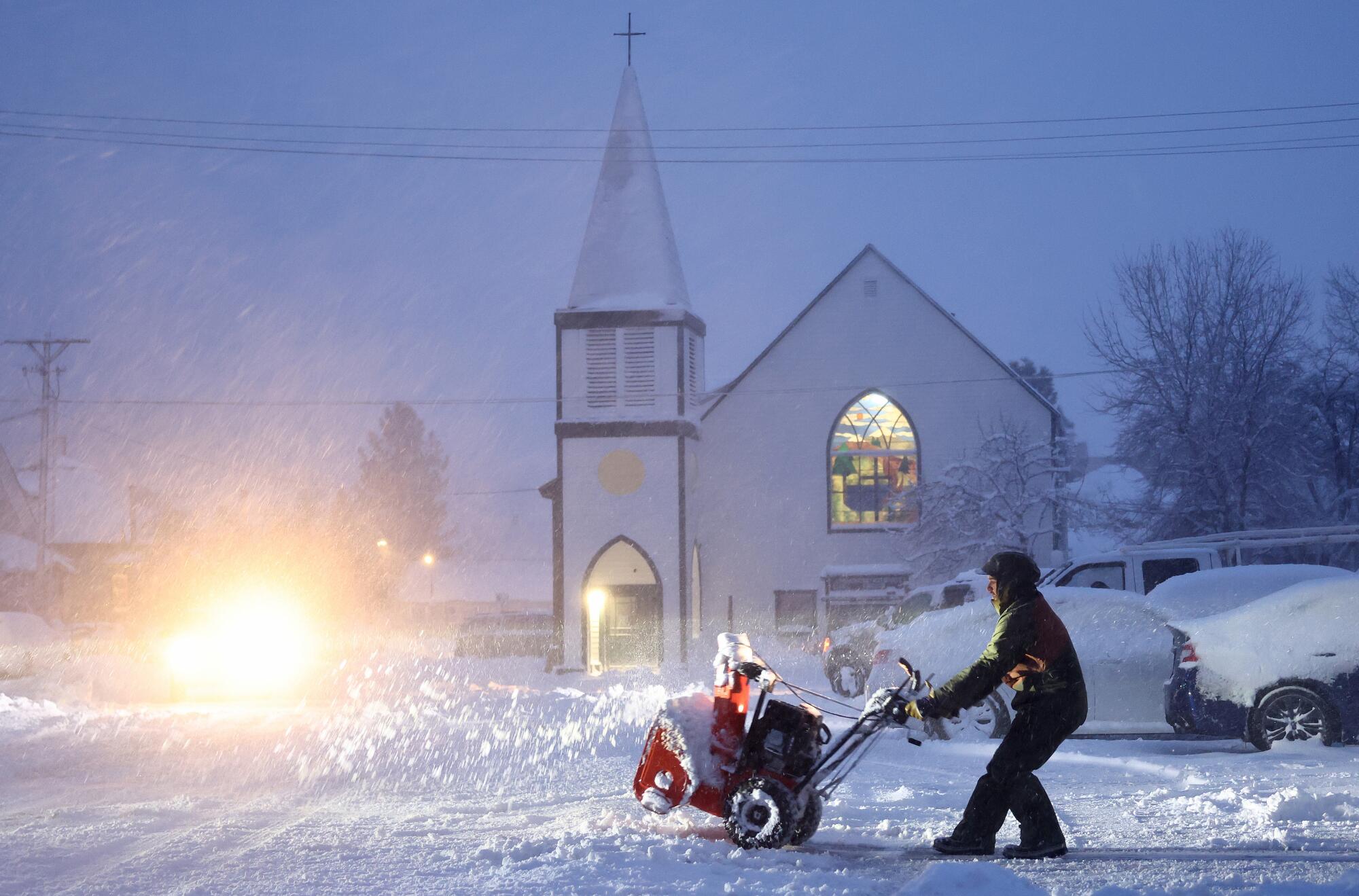 Michael Murray utilise une souffleuse à neige dans l'obscurité lors de fortes chutes de neige devant une église.