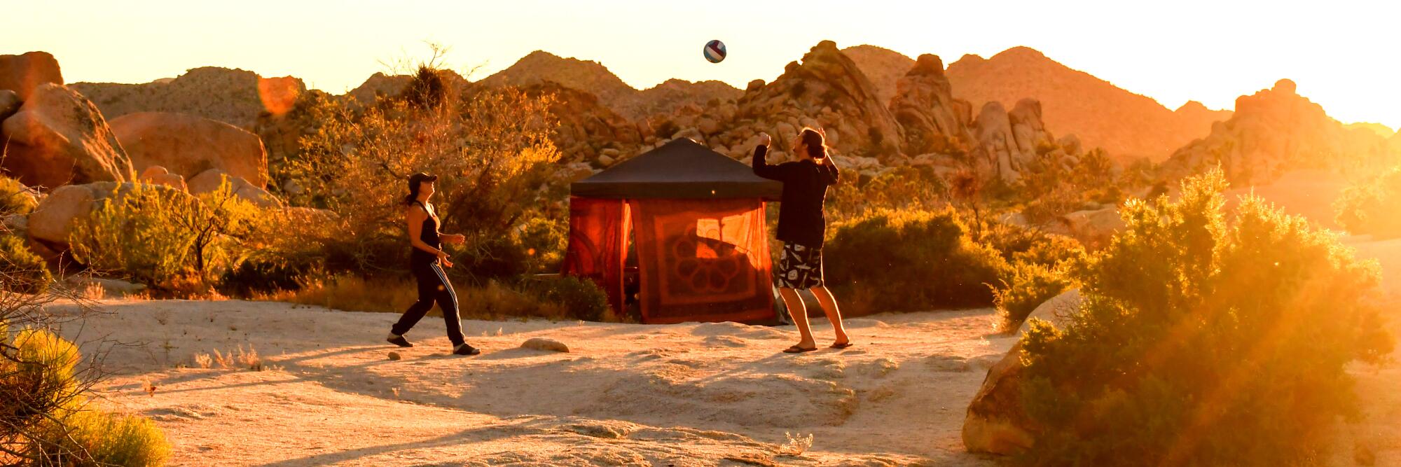 Jumbo Rocks Campground, Joshua Tree National Park, with people playing with a ball and a tent in front of rocky hills.