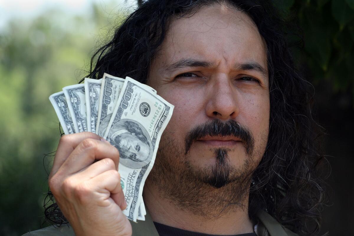 Robert Ramirez, 45, holds up $206 that he found in an envelope in a tree in the parking lot of the Huntington Library on Friday.