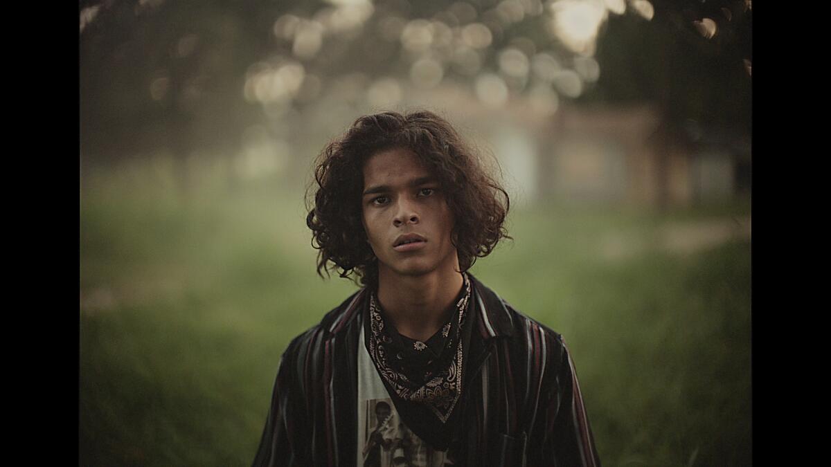 A teenager with a bandanna around his neck looks into the camera.