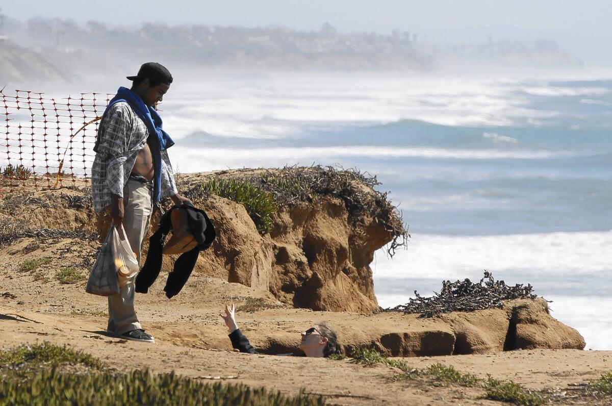 A couple climb down to the beach next to a section of bluff that has eroded in Carlsbad.