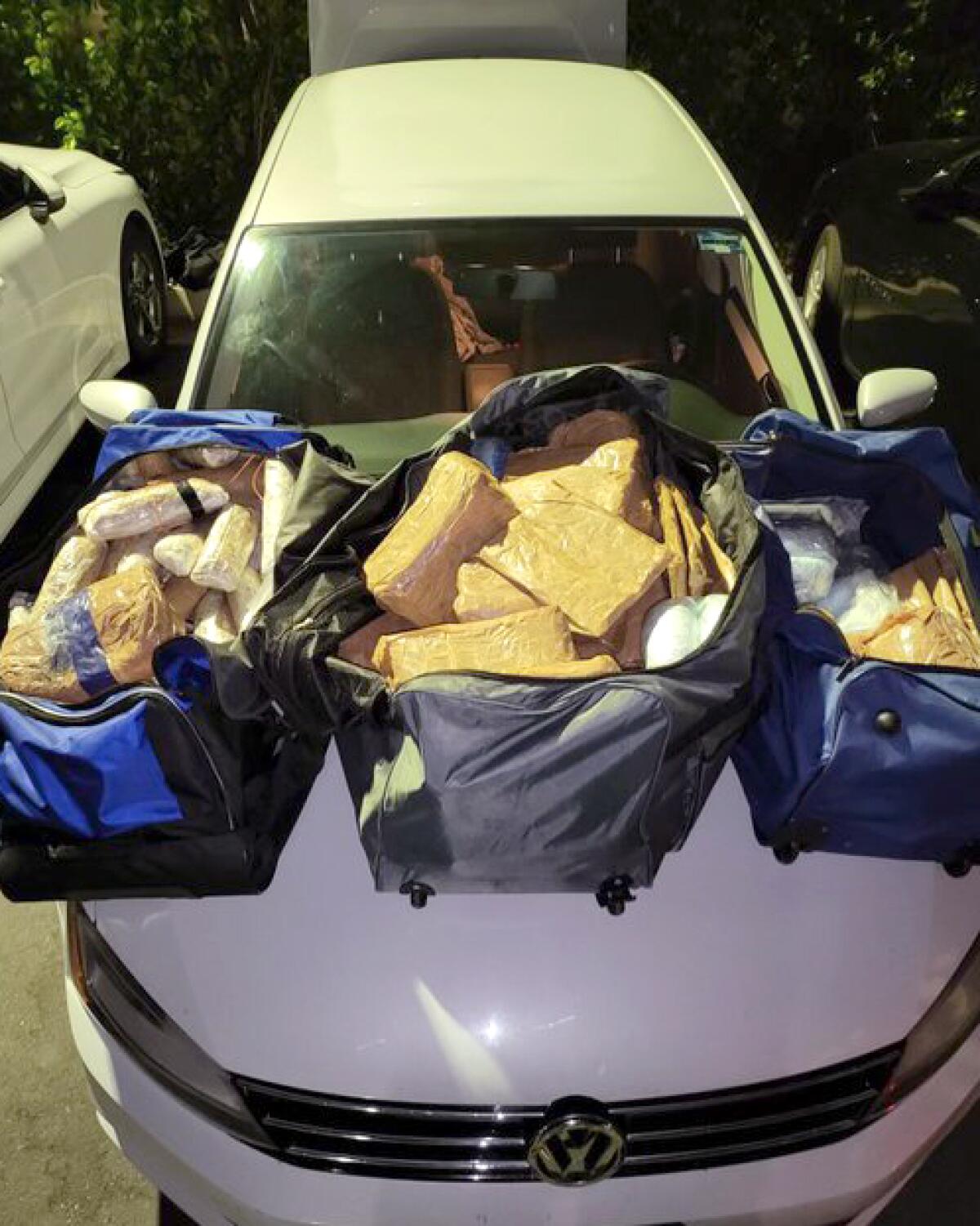 Three large duffel bags sit on the front hood of a Volkswagen Jetta