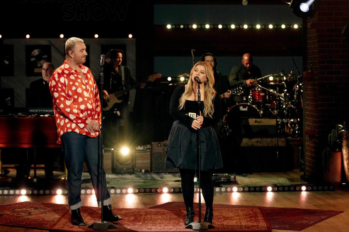 A person in a red shirt and jeans watching a woman in a black shirt and skirt singing on a stage.