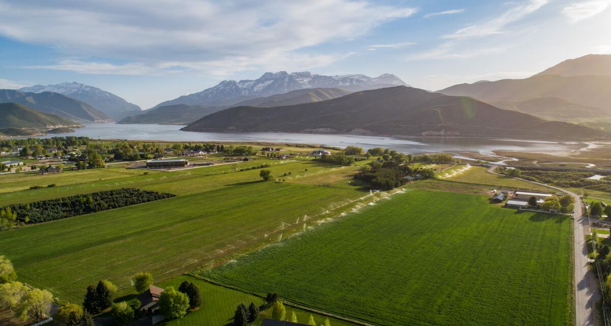 Aerial view of 30-acre ranch with buildings, open space and trees in front of mountains, valleys and rivers.