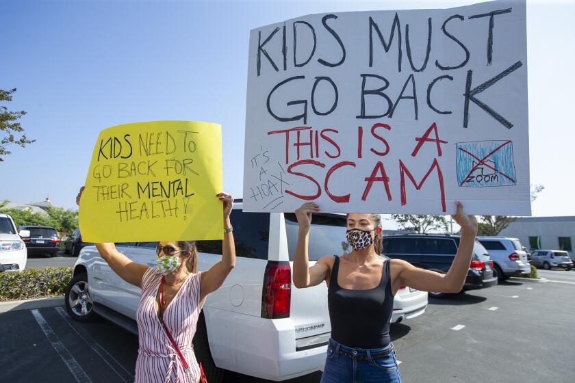 Julia Graham, left, and Karla Rivera hold sigs in protest outside of the Newport-Mesa Unified School District offices in Costa Mesa on Thursday, October 8.