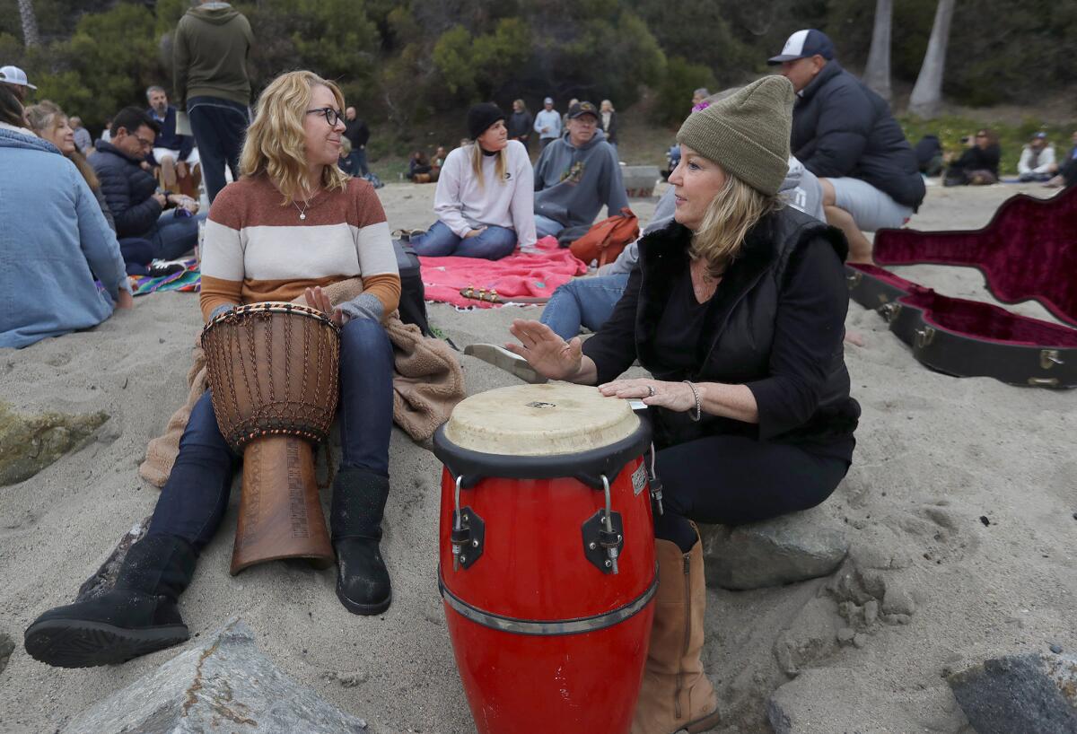 Michelle Barisoff and Mary Wynn, from left, join the drum circle remembrance at Aliso Beach in honor of Taylor Hawkins.