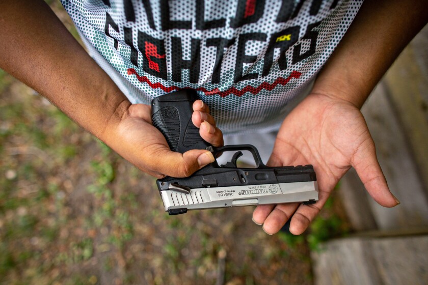 A person in a "Freedom Fighters" shirt holds a handgun.