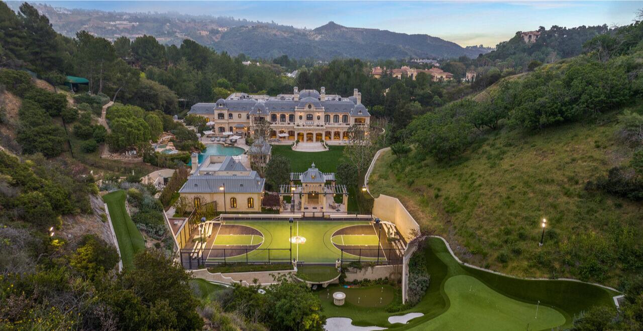 An aerial view of the estate with the mansion, basketball court and golf course surrounded by landscaping and hills.