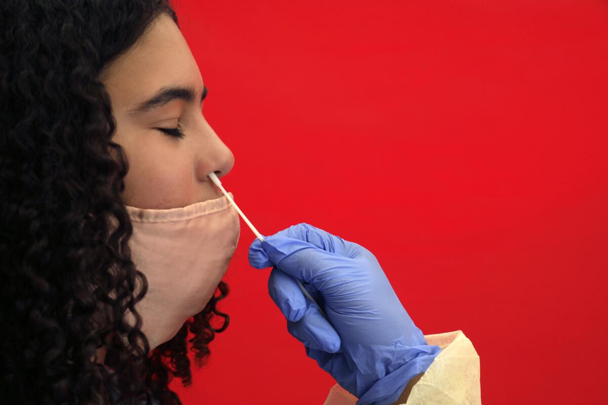 A gloved hand inserts a nasal test into a girl's nose