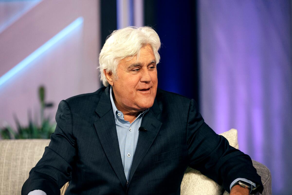 Jay Leno wearing a blue sportscoat and sitting in a chair