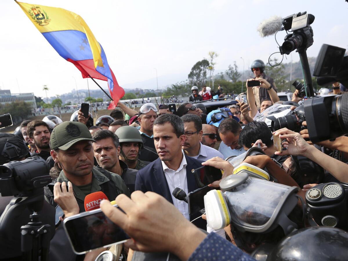 Venezuela's opposition leader and self-proclaimed president Juan Guaido, center, stands with an unidentified military officer who is helping to lead a military uprising, center left, as they talk to the press and supporters outside La Carlota air base in Caracas, Venezuela, Tuesday, April 30, 2019. GuaidÃ took to the streets with activist Leopoldo Lopez and a small contingent of heavily armed troops early Tuesday in a bold and risky call for the military to rise up and oust Maduro. (AP Photo/Fernando Llano)