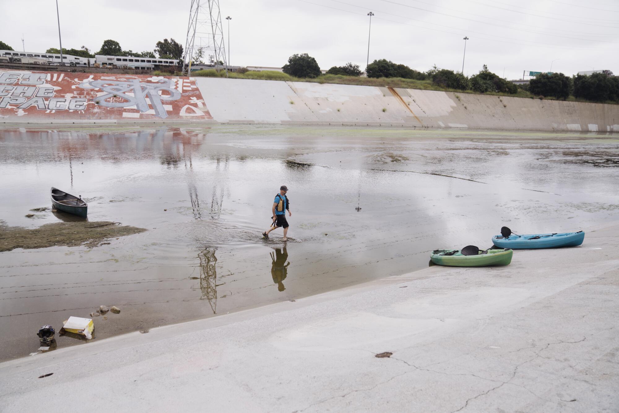 A man strides across a shallow section of the Los Angeles River.