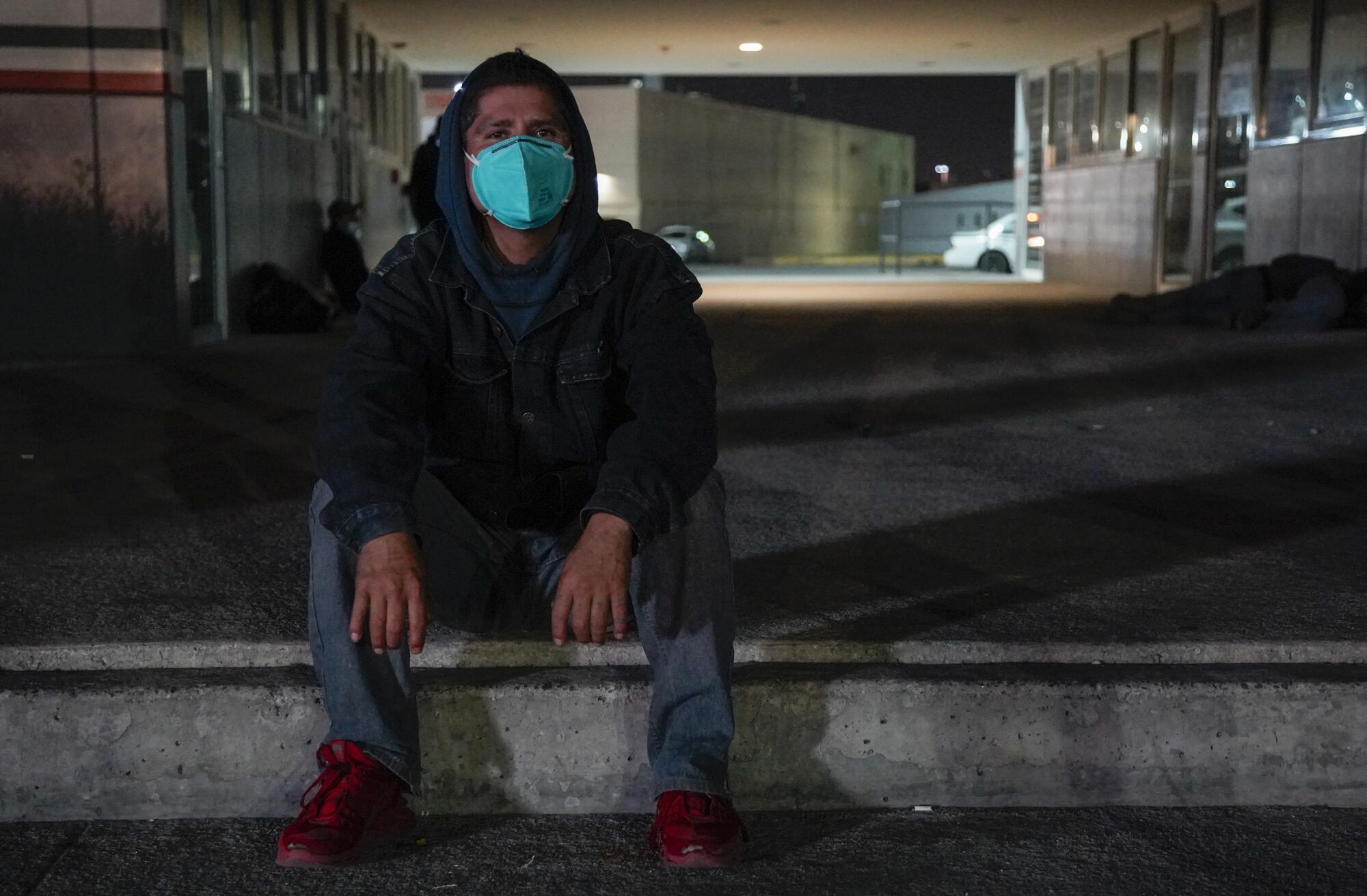 Enrique sits on the sidewalk in a small plaza by the Otay Mesa Port of Entry