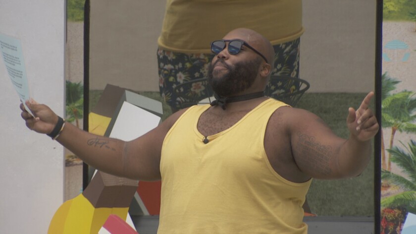 A man in a yellow tank top and sunglasses with his arms held open as if gesticulating
