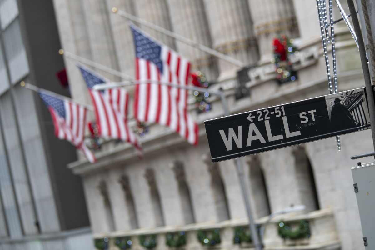 To the left of a Wall Street street sign are three U.S. flags flying outside the New York Stock Exchange. 